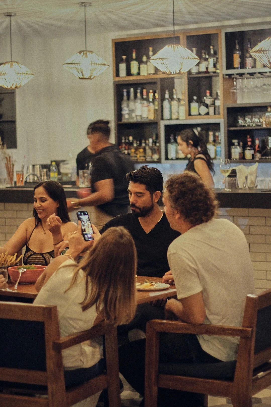 Comensales alrededor de una mesa de ICÚ, con la barra y las lámparas encendidas al fondo