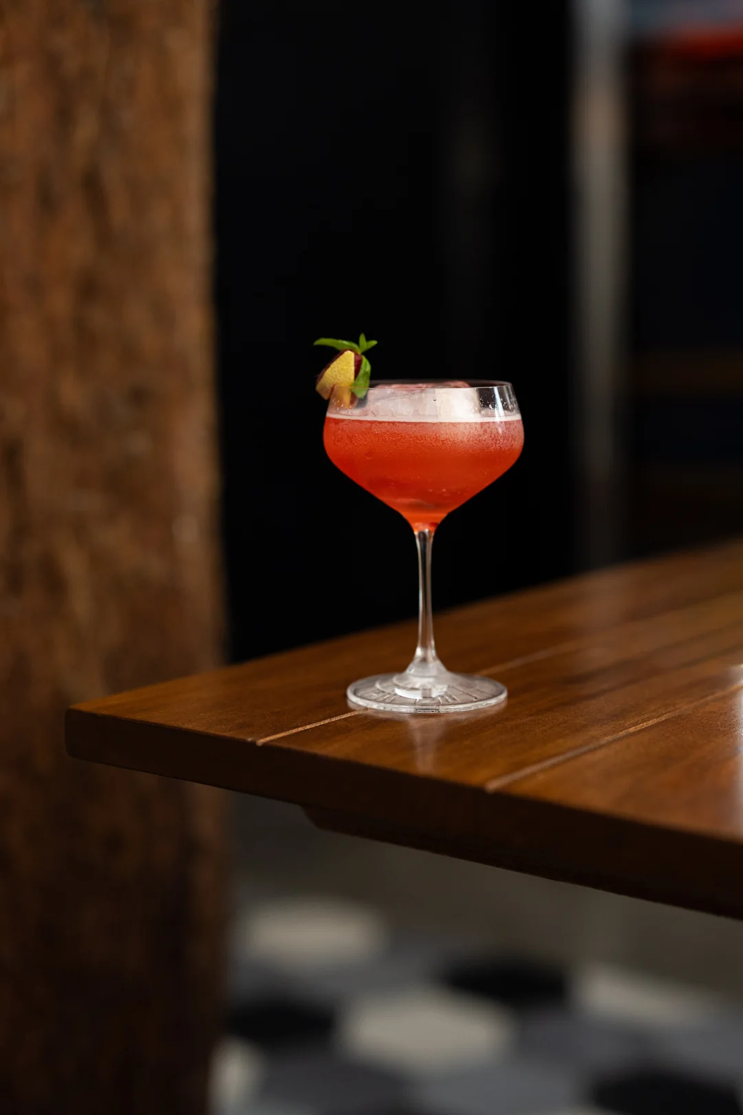Coctel rojizo en copa, sobre una mesa de madera en ICÚ