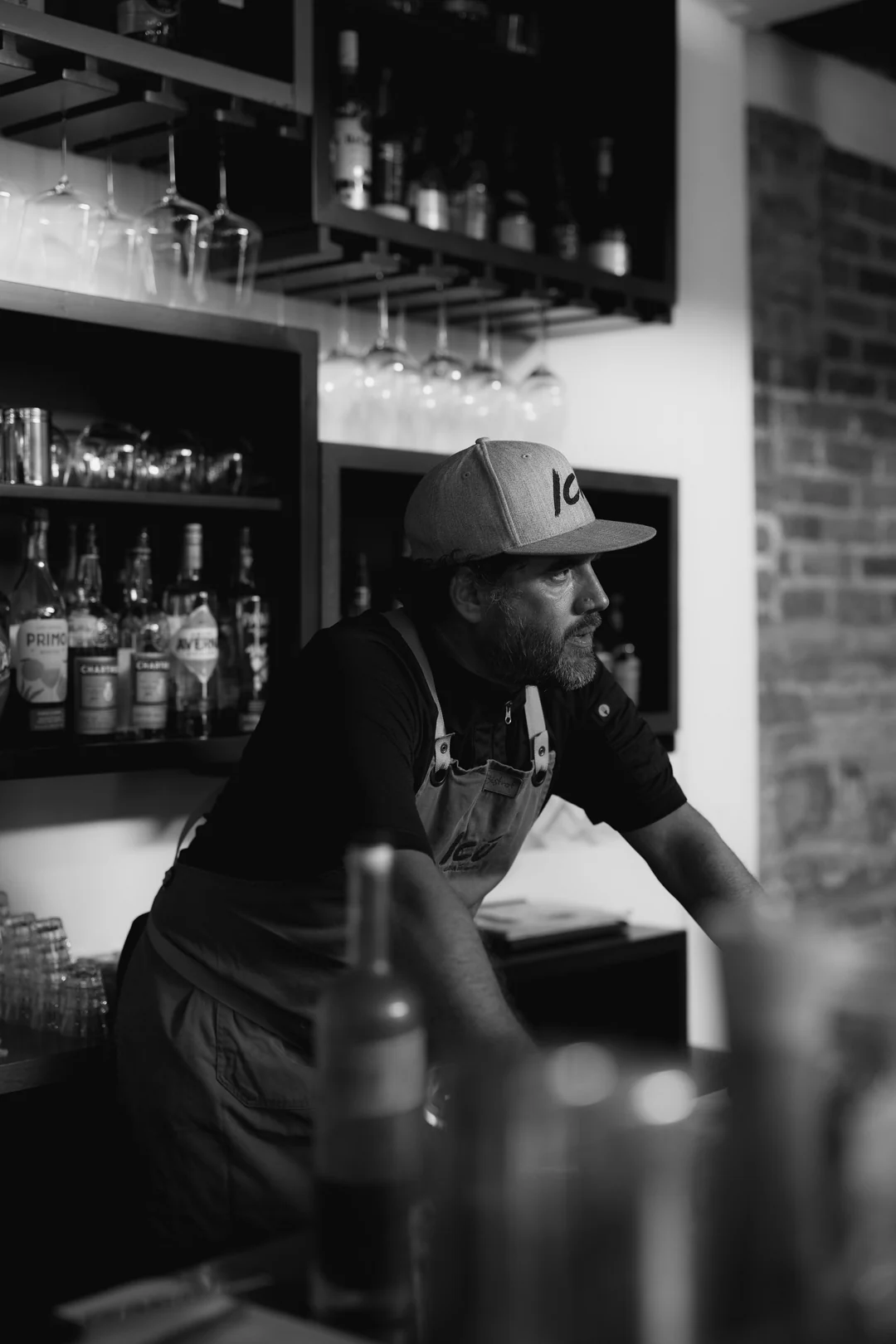 Mauricio Leal con gorra y mandil de ICÚ, apoyado en la barra; retrato en blanco y negro
