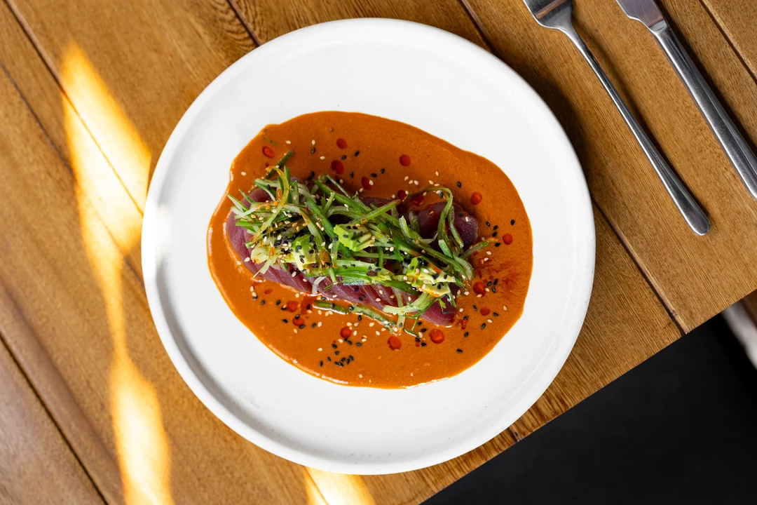 Platillo de ICÚ con salsa naranja, vegetales y semillas sobre un plato blanco